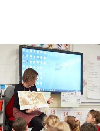 Adult reading a storybook to a group of pupils in a classroom, leading a shared reading and discussion activity.